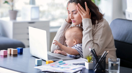 Gestresste Mutter im Homeoffice mit Kind auf dem Schoß