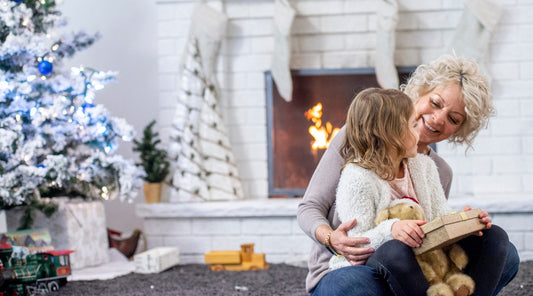 Oma und Enkelin mit Weihnachtsgeschenk vor Kamin und Tannenbaum