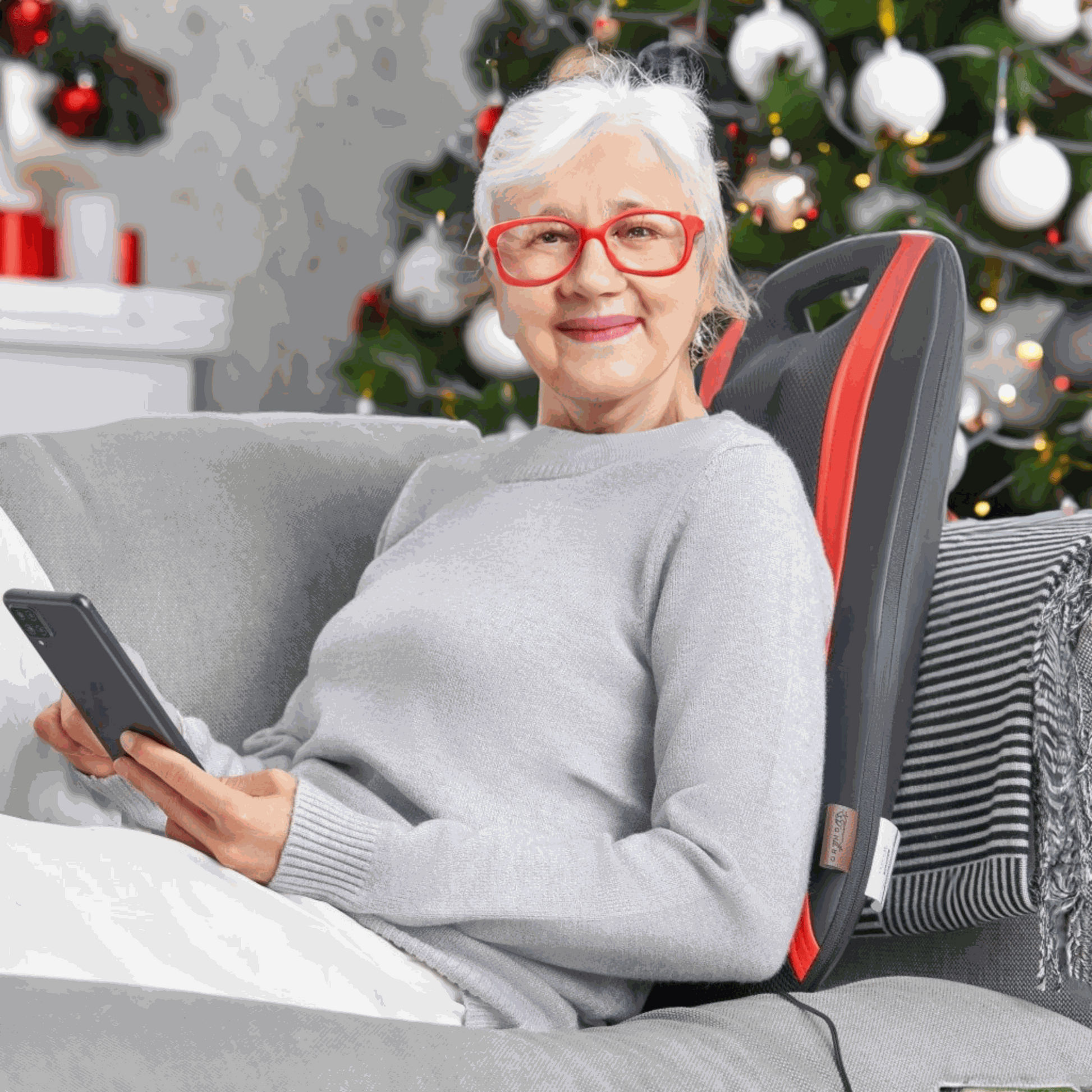 Ältere Frau entspannt mit OrthoMechanik Rücken-Massagegerät vor einem Weihnachtsbaum.