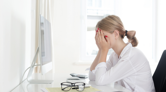 Gestresste Frau im Büro mit Erschöpfung am Schreibtisch – typisches Symptom von Burnout oder Bildschirmarbeit.