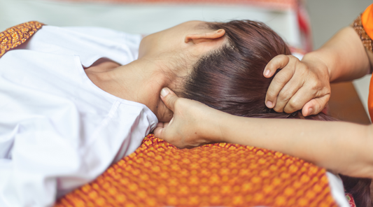 Eine Person liegt entspannt auf der Seite, während eine Massage oder Akupressurbehandlung im Nackenbereich durchgeführt wird. 