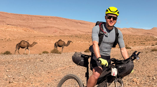 Ultracycling-Bikepacking-Radfahrer in der Wüste mit Kamelen im Hintergrund Atlas Mountain Race