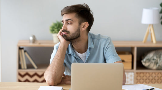 Gelangweilter Mann am Schreibtisch starrt gedankenverloren vom Laptop weg Bewegungsmangel