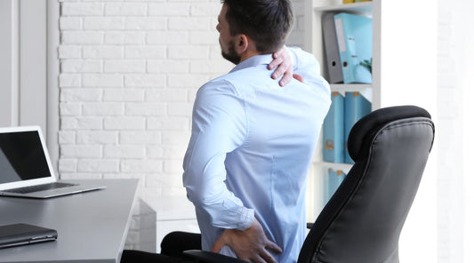 Mann mit Rückenschmerzen im Büro hält sich Nacken und Lendenbereich wegen schlechter Sitzhaltung