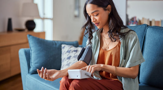 Frau misst ihren Blutdruck mit einem digitalen Blutdruckmessgerät auf dem Sofa