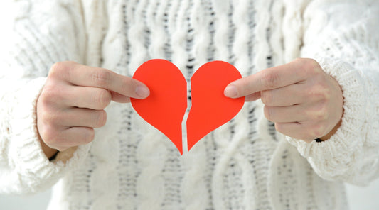 Hände halten ein gebrochenes rotes Papierherz