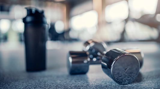 Zwei Chrom-Hanteln mit Shakerflasche im Fitnessstudio effektive Workouts