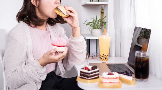 Frau isst Fast Food und Desserts am Schreibtisch