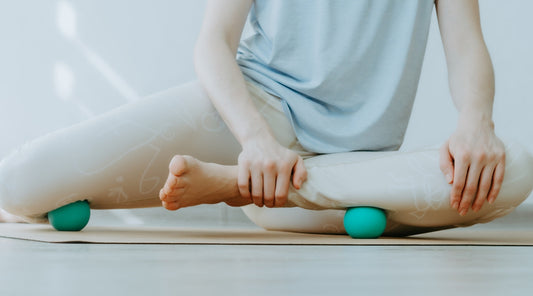 Person bei Faszienmassage mit Massagebällen im Sitzen auf Yogamatte