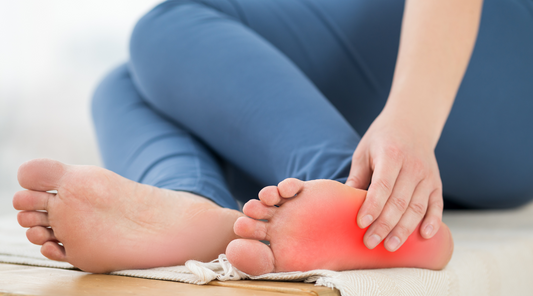 Person hält schmerzenden Fuß, rote Markierung hebt den Schmerzbereich an der Fußsohle hervor.
