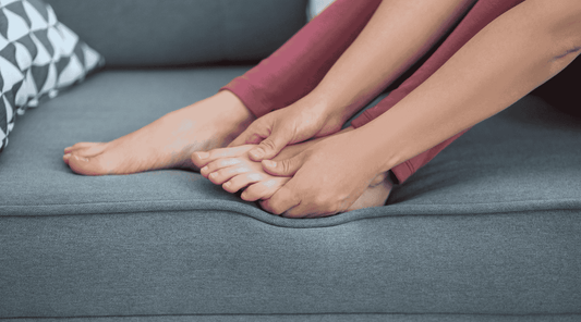 Nahaufnahme von Füßen auf einem Sofa, eine Person massiert den schmerzenden Fuß mit beiden Händen – mögliche Linderung bei Beschwerden wie einem Fersensporn