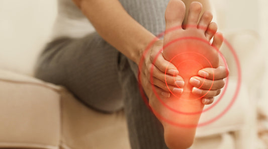 Frau hält schmerzenden Fuß mit hervorgehobener Schmerzstelle – typisches Symptom bei Plantarfasziitis oder Überlastung