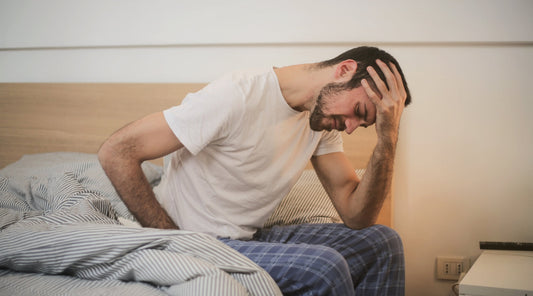 Mann mit morgendlichen Kopfschmerzen sitzt erschöpft am Bettrand