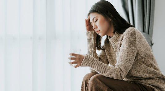 Junge Frau mit Kopfschmerzen hält ein Glas Wasser in der Hand