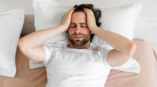 Mann liegt mit starken Kopfschmerzen im Bett und hält sich den Kopf