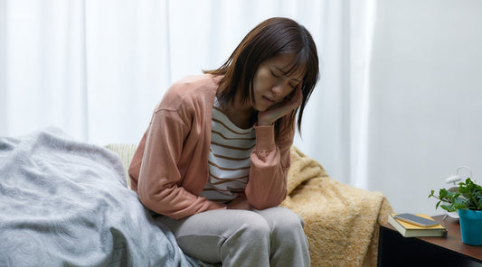 Junge Frau mit Kopfschmerzen sitzt erschöpft auf dem Bett