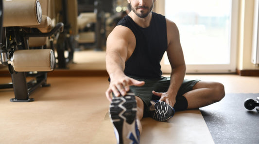 Mann im Fitnessstudio macht Dehnübung für Beinmuskulatur – Stretching nach dem Krafttraining