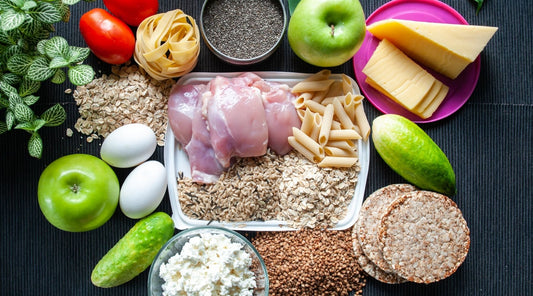 Ausgewogene Ernährung für Muskelaufbau: Haferflocken, Hähnchen, Eier, Käse, Pasta und Gemüse auf einem Tisch arrangiert