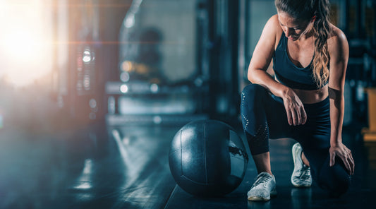 Sportlerin erholt sich nach intensivem Krafttraining im Fitnessstudio mit Medizinball – Fokus auf Regeneration und Muskelaufbau