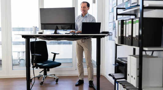 Mann arbeitet im Stehen an höhenverstellbarem Schreibtisch – ergonomischer Arbeitsplatz zur Prävention von LWS-Beschwerden