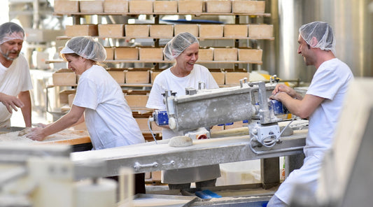 Bäckereimitarbeitende stehen bei der Arbeit an Maschinen und Arbeitsflächen