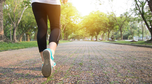 Frau beim Joggen im Park auf Kiesweg bei Sonnenaufgang – gesunde Laufbewegung von hinten