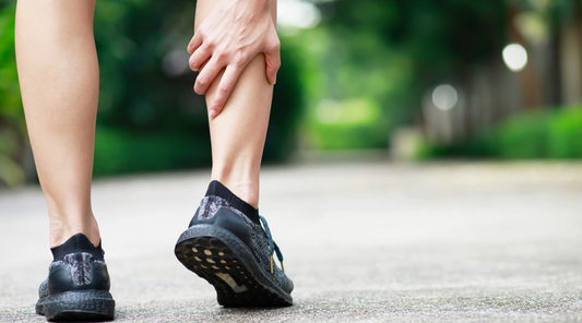 Läufer greift sich an die Wade wegen Muskelkater oder Wadenkrampf beim Joggen im Freien