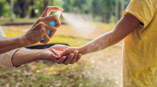 Erwachsene Hand sprüht Mückenspray auf Kinderarm zum Schutz vor Insektenstichen im Sommer