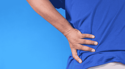 Eine Person in einem blauen T-Shirt hält sich den unteren Rücken mit der Hand, möglicherweise aufgrund von Rückenschmerzen oder Verspannungen, vor einem blauen Hintergrund.