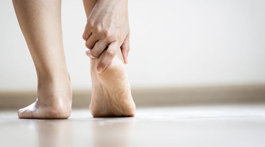 Frau greift sich an schmerzende Ferse – typisches Symptom bei Plantarfasziitis
