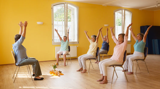 Seniorinnen machen Stuhlyoga in heller Gruppenstunde