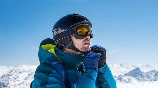 Skifahrer setzt Helm und Skibrille an sonnigem Wintertag in den Bergen auf