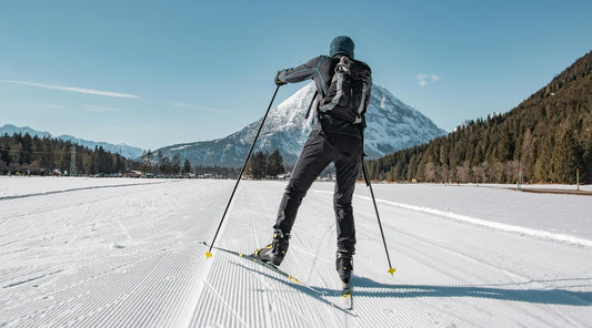 Langläufer auf gespurter Loipe mit Blick auf verschneiten Berg und Wald