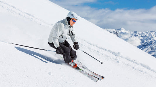 Skifahrer in weißer Jacke fährt auf verschneiter Piste – Belastung für den Rücken
