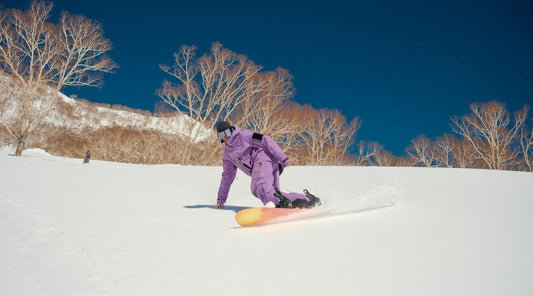 Snowboarder in lila Anzug fährt im Schnee mit Hand am Boden Wintersport Action