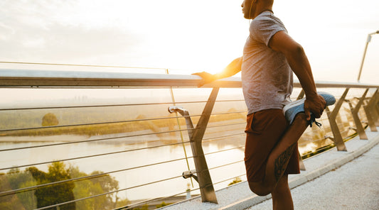 Mann dehnt Beinmuskulatur vor dem Joggen bei Sonnenaufgang