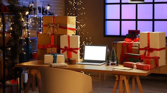 aptop auf Schreibtisch umgeben von vielen Weihnachtsgeschenken.