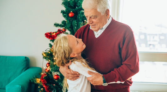 Enkelin umarmt ihren Großvater vor Weihnachtsbaum
