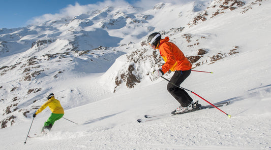 Zwei Skifahrer fahren eine verschneite Piste hinab